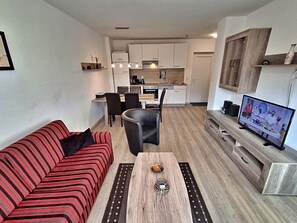 Een ruimtelijk ingerichte leefruimte met kitchenette, een eethoek en een zithoek met een bank en salontafel.