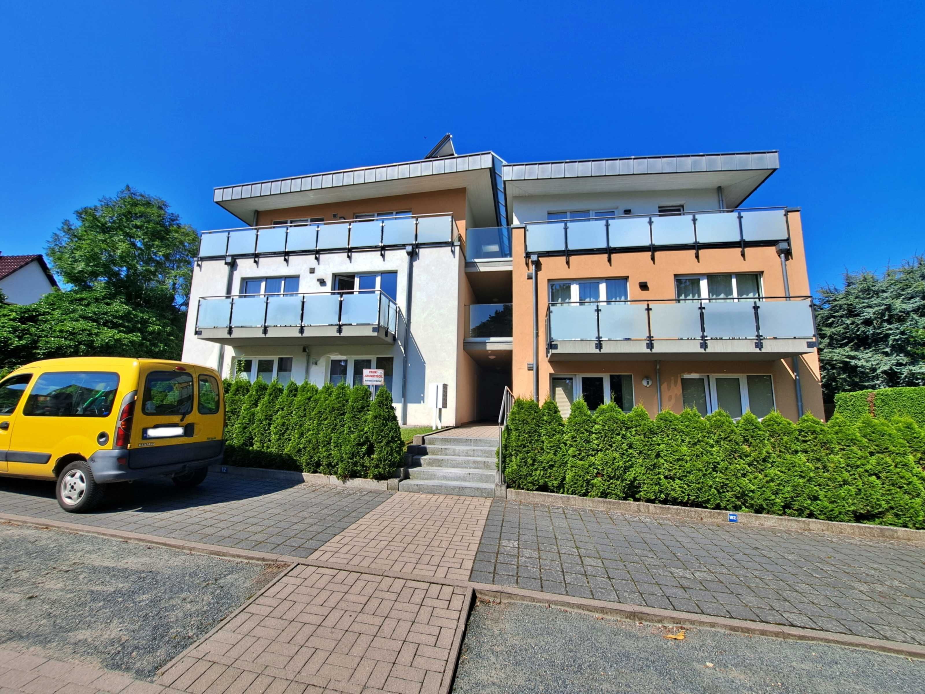 Ein modernes, zweistöckiges Gebäude mit Flachdach und großen Fenstern, vor der Fassade ein gelber Wagen.
