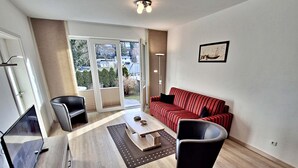 Un salon moderne avec un canapé à rayures rouges, un fauteuil noir, une table basse en bois et un meuble TV en verre.