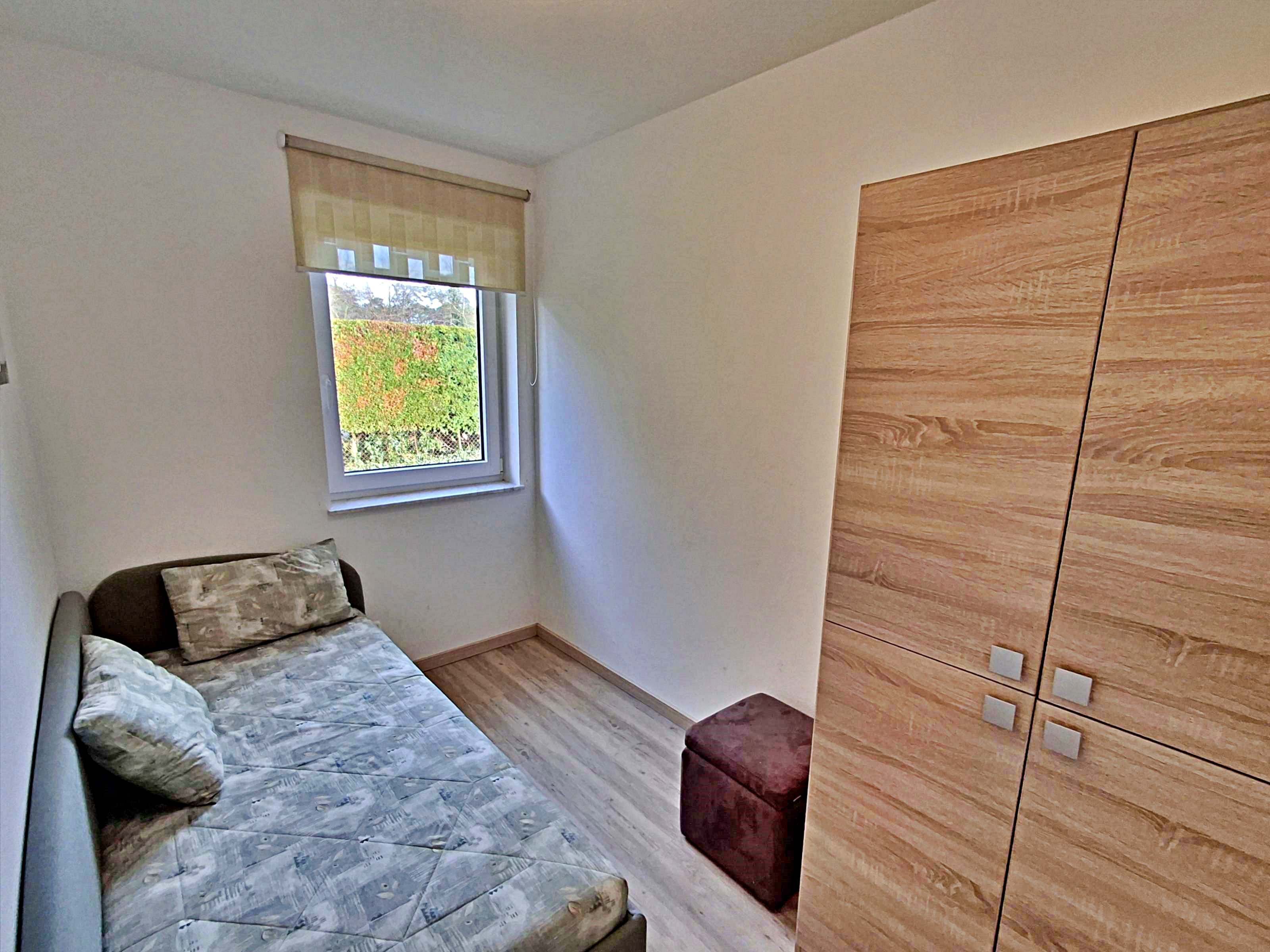 Un dormitorio pequeño con cama, ventana con vistas a la vegetación y armario de madera.