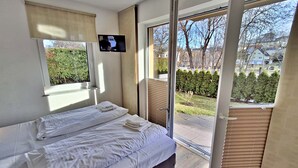 Une chambre à coucher avec un lit, un téléviseur fixé au mur et une porte-fenêtre coulissante donnant sur un balcon.