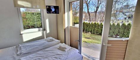 A bedroom with a bed, a TV mounted on the wall, and a sliding glass door leading to a balcony.