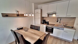 Une cuisine moderne avec des meubles blancs, une table à manger en bois et un four encastré.
