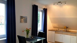 A compact kitchen with a dining area, featuring a small table, chairs, a vase with flowers, and a window with curtains. - Apartment 2 - Cozy in the attic - Apartment Burgert Family (Patzig)