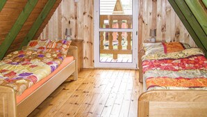 A cozy attic bedroom with two wooden beds, a wooden floor, and a view of a traditional house through a wooden door.