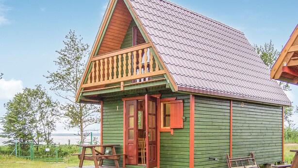 A small, single-story wooden cabin with a green exterior, a red door, and a balcony with a railing.