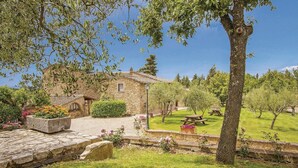Une maison en pierre avec un jardin, des tables de pique-nique et un ciel dégagé.