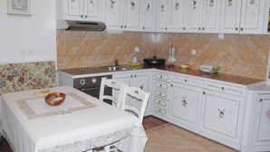 A kitchen with white cabinets, a stove, a sink, and a table with a floral tablecloth. - Holiday apartment near the beach with air conditioning (Baška)