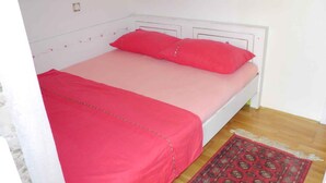 A bed with a white frame, red bedding, and a patterned rug on a wooden floor. - Holiday apartment near the beach with air conditioning (Baška)