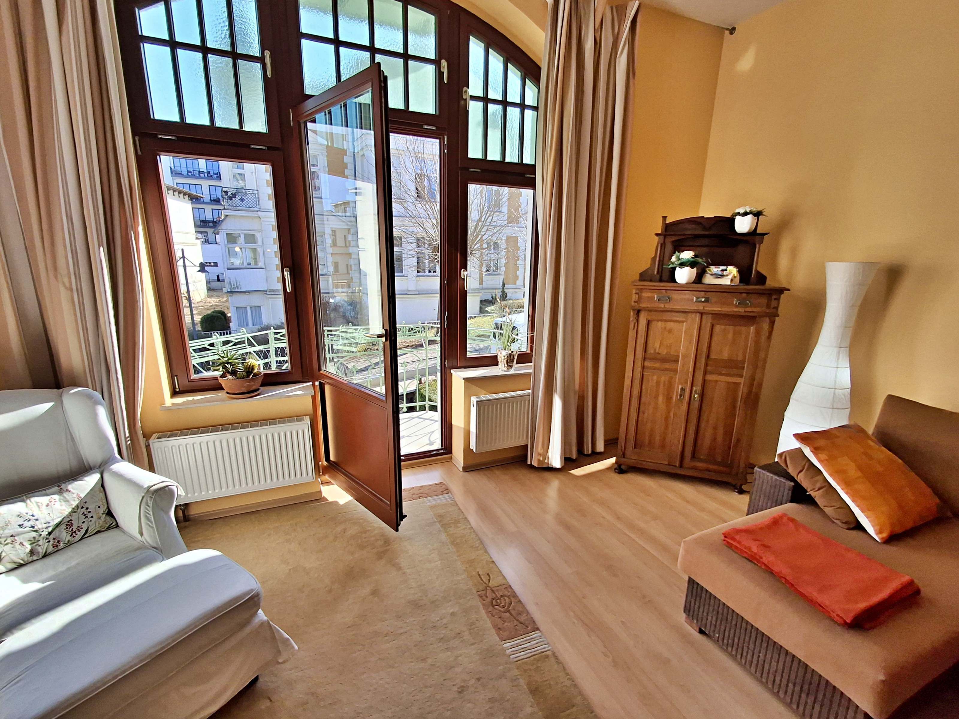A living room with a sofa, a wooden cabinet, and a view of the outside through large windows.