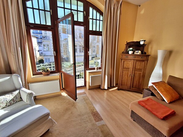 A living room with a sofa, a wooden cabinet, and a view of the outside through large windows.