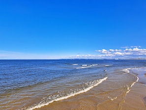 A beach with clear blue water, waves, and a distant ship.