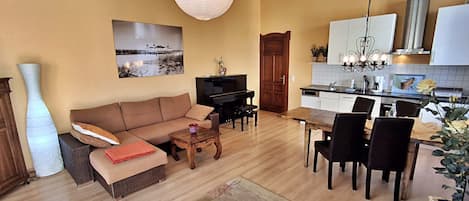 A living room with a sofa, coffee table, and TV, a dining area with chairs and a table, and a kitchen with cabinets and a sink.