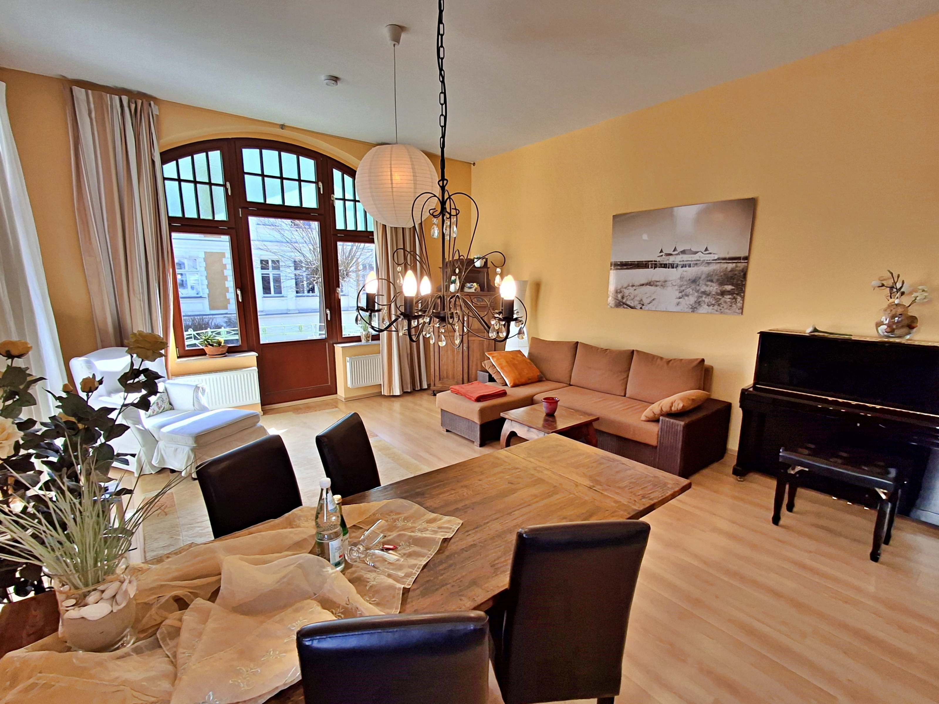Un amplio salón con zona de comedor, un piano y un gran ventanal con cortinas.