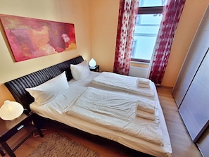 A neatly made bed with white linens and pillows, a bedside lamp, and a painting on the wall.
