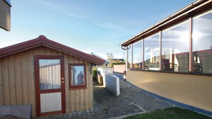 Eine kleine Holzhütte mit rotem Dach und Glastür, neben einem größeren Gebäude mit großen Fenstern.