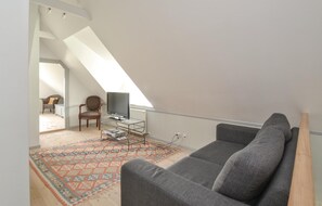 Cozy attic retreat with a sofa, chair, and entertainment unit, offering a view of the adjacent living area.