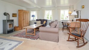 Ett mysigt vardagsrum med en soffa, en gungstol, ett bord och en öppen spis.