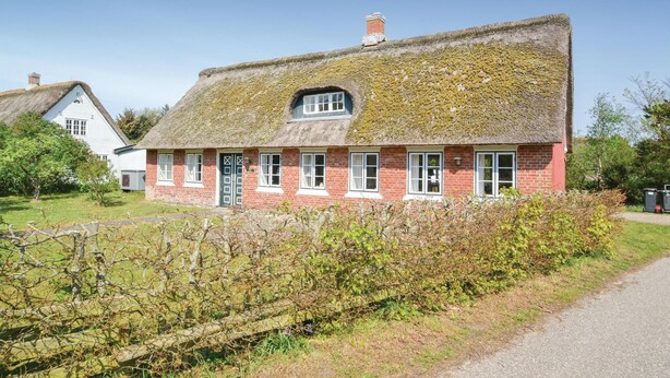 Ett traditionellt hus med röda tegelväggar, halmtak och vita fönsterramar.