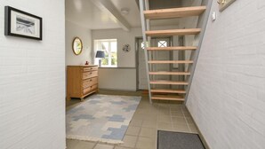 En smal hall med en trästege, en byrå, en spegel och en inramad tavla på väggen.