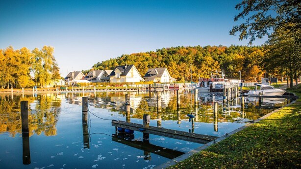 Un lac paisible avec un quai, des bateaux et des maisons en arrière-plan.