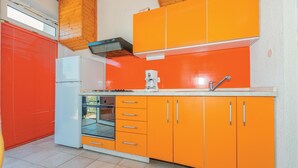 Een compacte keuken met oranje kastjes, een witte koelkast, een koffiezetapparaat en een ingebouwde oven.