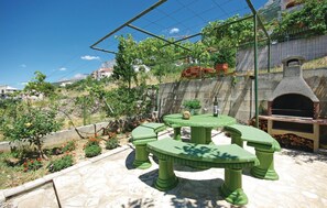 Eine Terrasse mit einem grünen Tisch und Stühlen, einer Steinmauer und einem Backofen aus Ziegeln.
