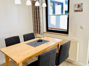 Ein Essbereich mit Holztisch, vier Stühlen, gemusterten Vorhängen, einem Fenster mit Jalousien und einer Heizung.