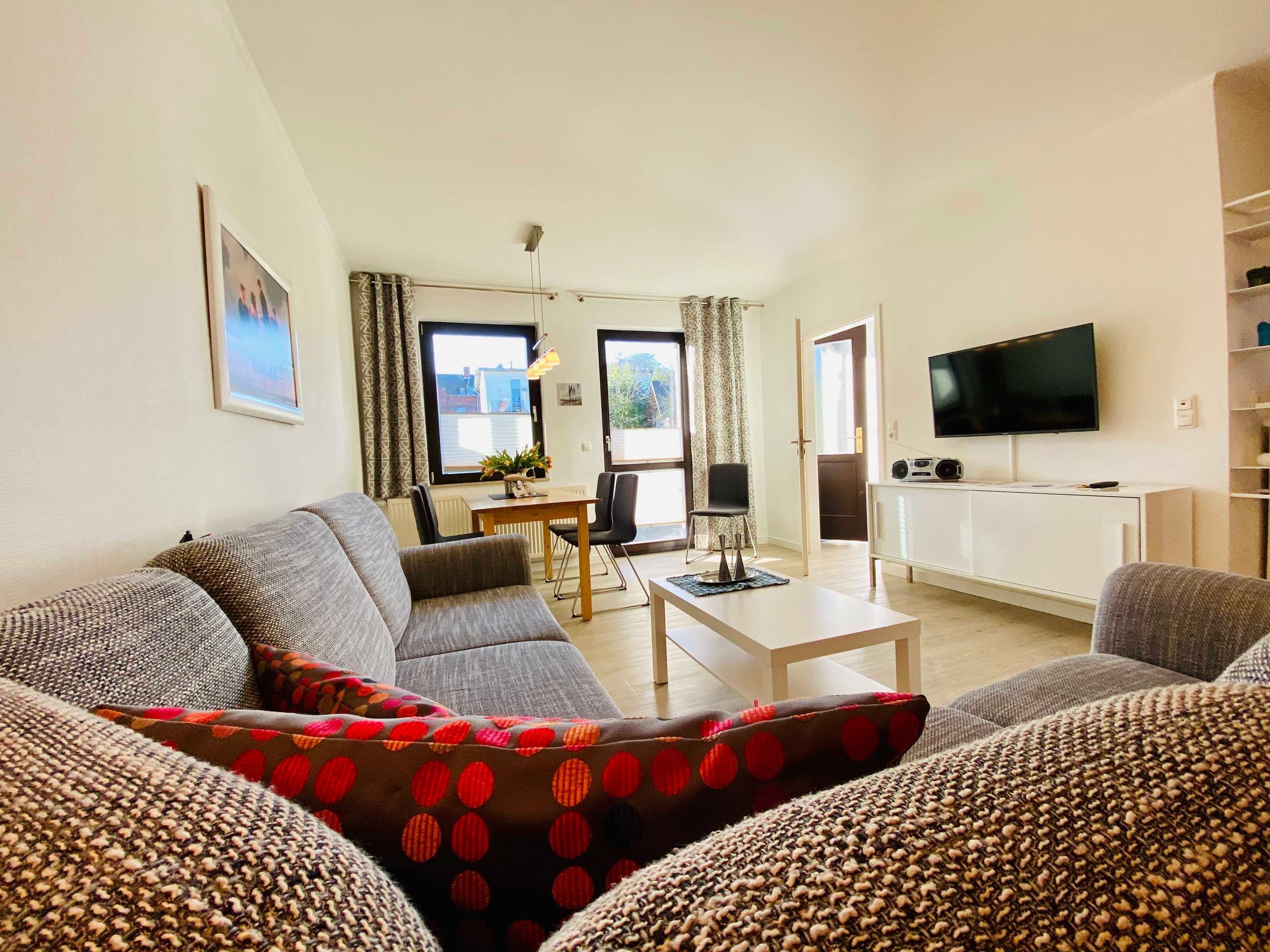 A living room with a sofa, a coffee table, a TV, and a dining area with a table and chairs.