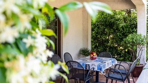 An outdoor patio with a table and chairs, surrounded by greenery.