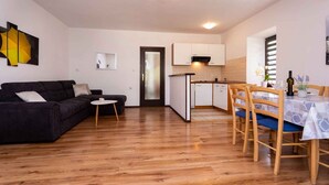 A compact living space with a dark-colored sofa, a small round table, a dining area with a table and chairs, and a kitchen with cabinets and a countertop.