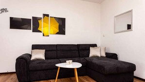 A modern living room with a black sectional sofa, a small white table, and three abstract wall art pieces.