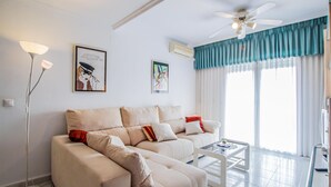 A living room with a beige sofa set, a glass coffee table, a standing floor lamp, and a ceiling fan. - Nice apartment in Arenales del Sol with swimming pool (Arenales del Sol)