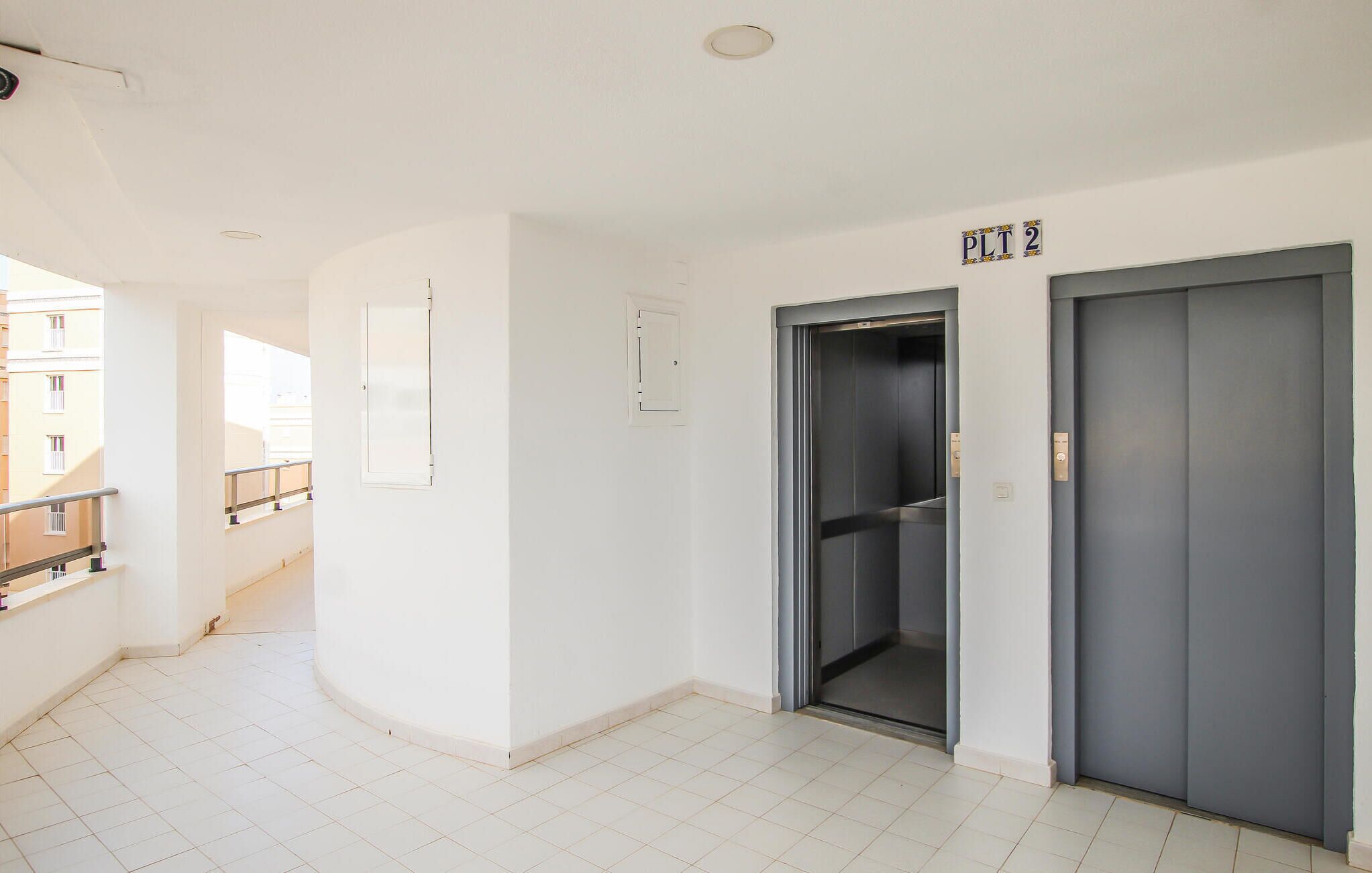 A clean, modern hallway with two elevators, a visible door, and a tiled floor.