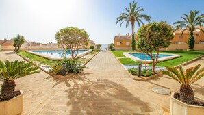 A pool area with two swimming pools, palm trees, and a paved walkway leading to a building. - Nice apartment in Arenales del Sol with swimming pool (Arenales del Sol)