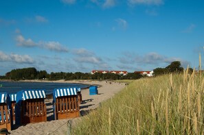 A beach with beach huts, a sandy shore, and a row of houses in the background.