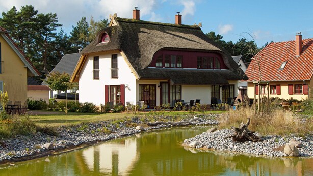 Une maison traditionnelle avec un toit de chaume, un étang et un jardin bien entretenu.