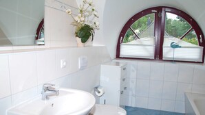 Une salle de bain avec un lavabo blanc, des toilettes et une fenêtre donnant sur une maison.