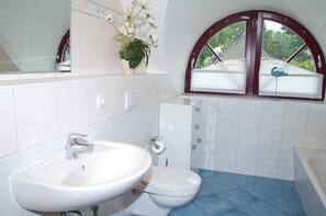 Een badkamer met een witte wastafel, toilet en een raam met uitzicht op een huis.
