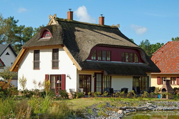 A traditional house with a thatched roof, a garden with a pond, and outdoor seating.