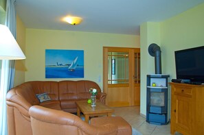 A living room with a brown leather sofa, a wooden coffee table, a television, and a painting on the wall.