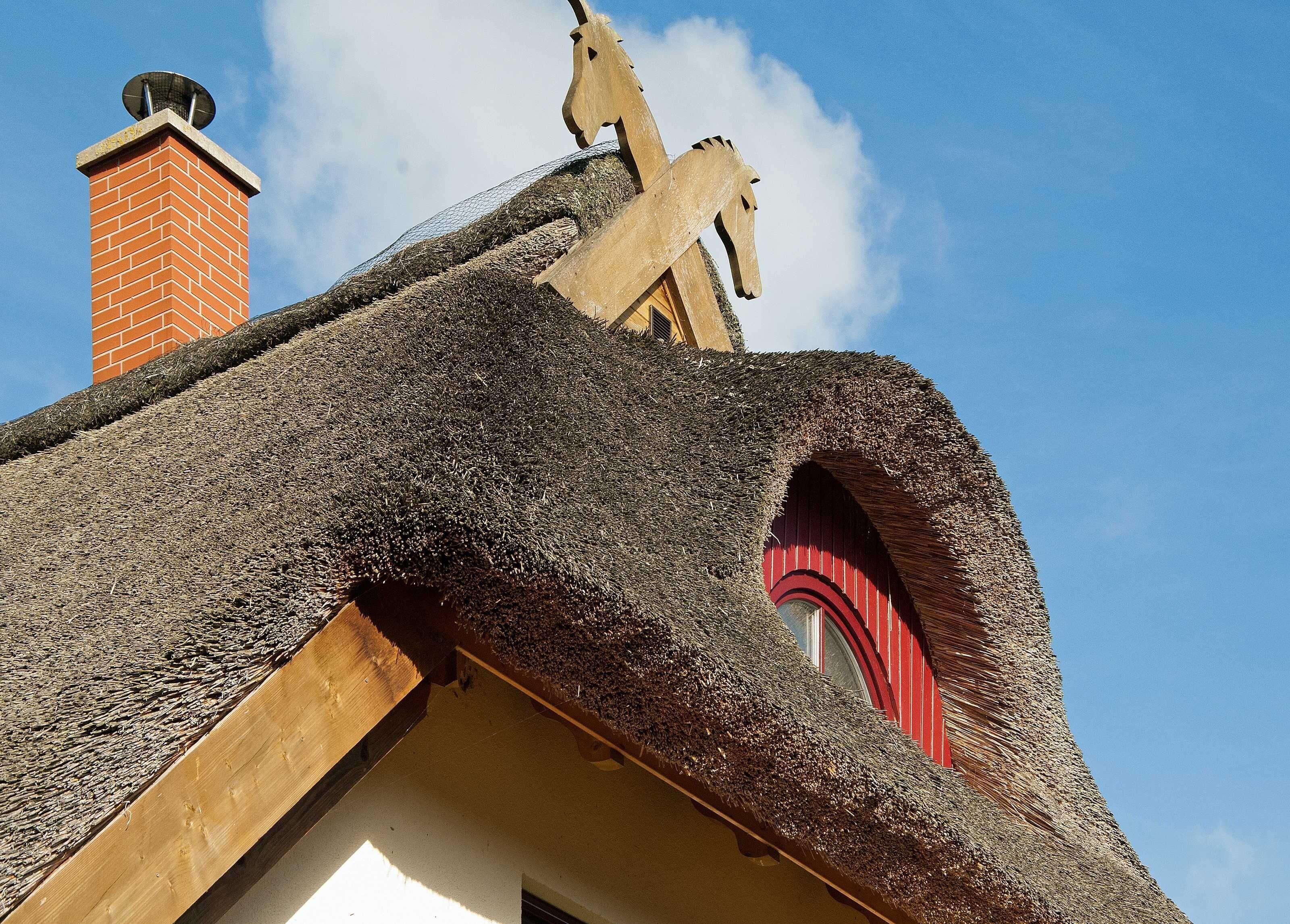 A building with a thatched roof, a brick chimney, and a distinctive red window arch.