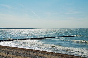 A beach with waves, a wooden jetty, and a clear sky.