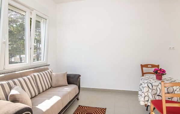 Quarto com sofá, mesa de jantar com cadeira e janela com vista para árvores.