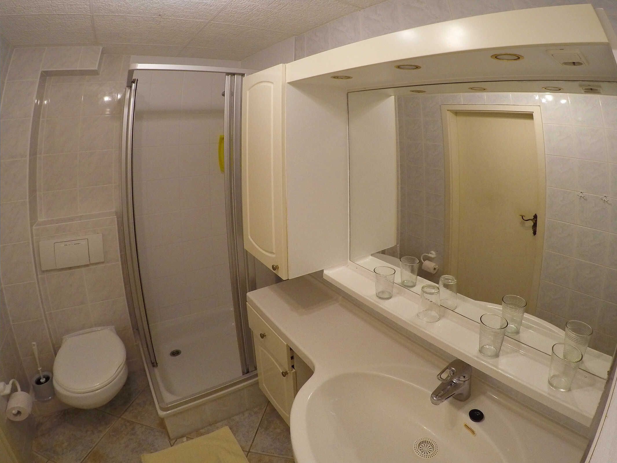 A bathroom with a shower, toilet, sink, and mirror.