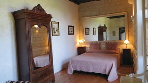 Een slaapkamer met een grote spiegel, twee nachtkastjes, een bed met een roze deken en houten vloeren.