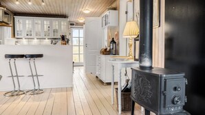 A kitchen with wooden cabinets, a black stove, and a dining area with a table and chairs. - Cozy home in Ebeltoft with kitchen (Ebeltoft)