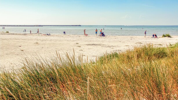 A beach with people sunbathing and swimming, and a rocky outcrop in the distance. - Cozy home in Ebeltoft with kitchen (Ebeltoft)