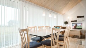 A modern dining area with a wooden table and chairs, a television, and a view of the outdoors through large windows. - Beautiful home in Brovst with sauna (Brovst)