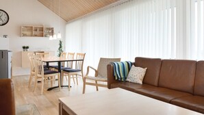 A modern living room with a wooden ceiling, a dining area with a table and chairs, a sofa, and a large window with blinds. - Beautiful home in Brovst with sauna (Brovst)